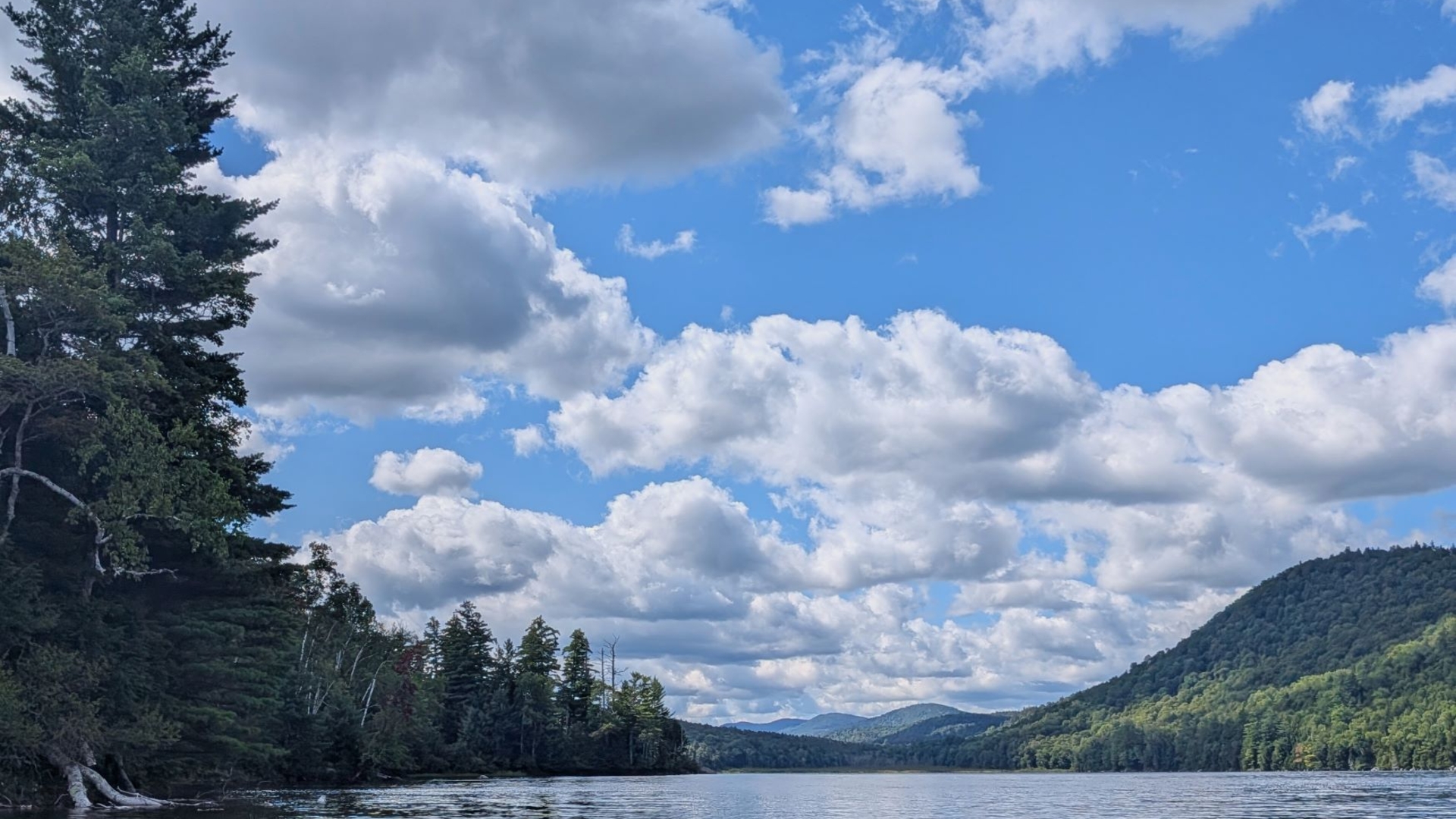 The view looking South from the middle of 13th lake in the middle of summer with green mountains, blue skies, and chrome-hued waters.